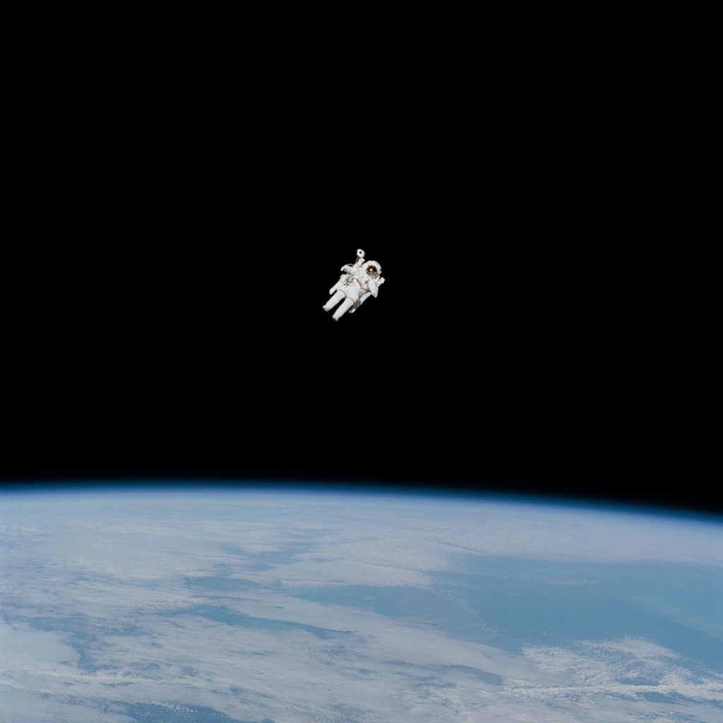Astronautti liitelee yksin pimeässä avaruudessa. Taustalla, alapuolella näkyy maapallon pintaa.